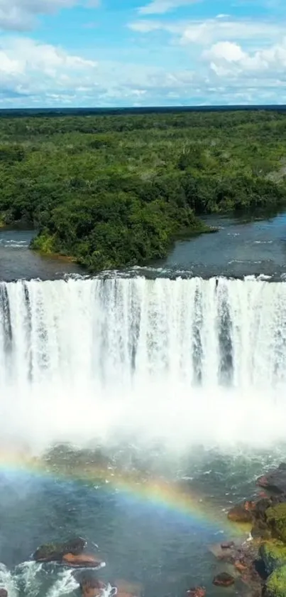 Waterfall with rainbow over lush green forest.