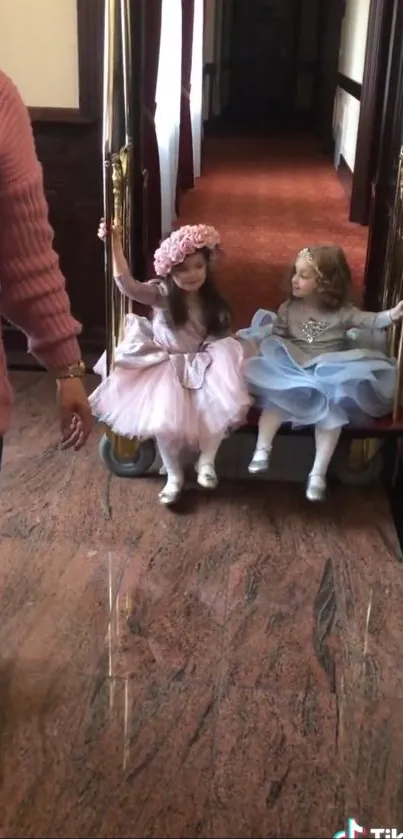 Two young girls in dresses enjoying a playful moment indoors.