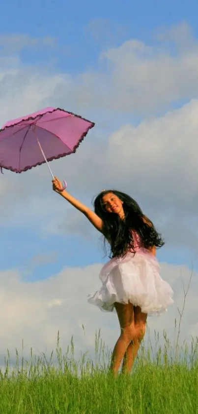 Girl with pink umbrella dancing in green field under blue sky.