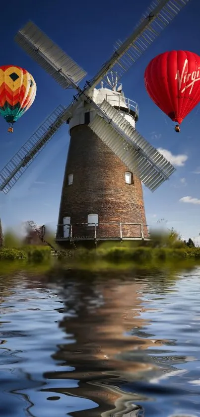 Windmill with hot air balloons reflecting on water under a blue sky.