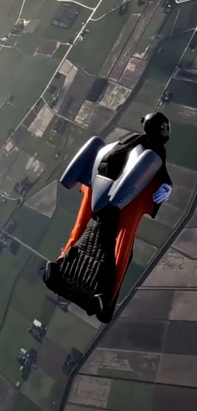 Person in wingsuit diving over vast landscape with fields below.