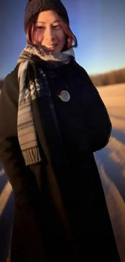 A person in winter attire stands on a snowy path as the sun sets in the background.