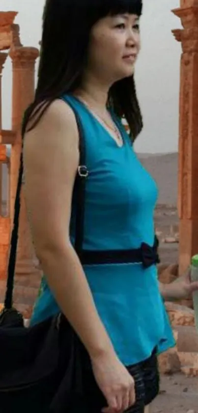 Woman in blue top standing by ancient ruins with a scenic view.