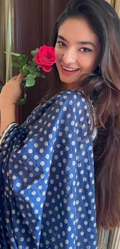 Woman in blue saree smiling with a red rose.