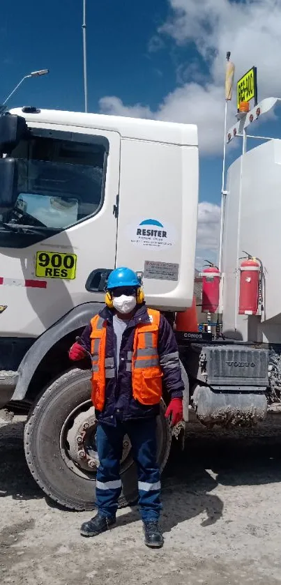 Worker in safety gear stands beside a transport truck on a clear day.