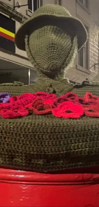 Yarn-covered sculpture on red postbox in city street at night.