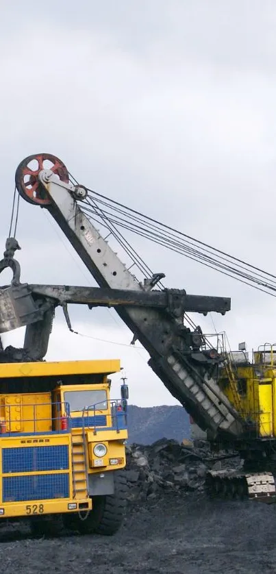 Yellow excavator and truck in mining site under a cloudy sky.