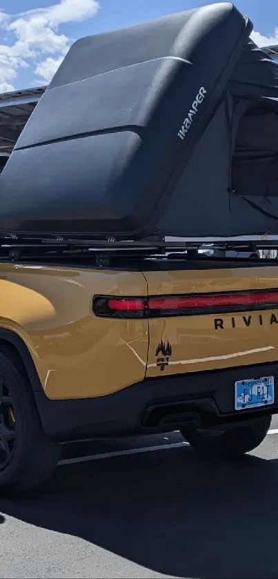 Yellow Rivian truck with camper shell under blue sky