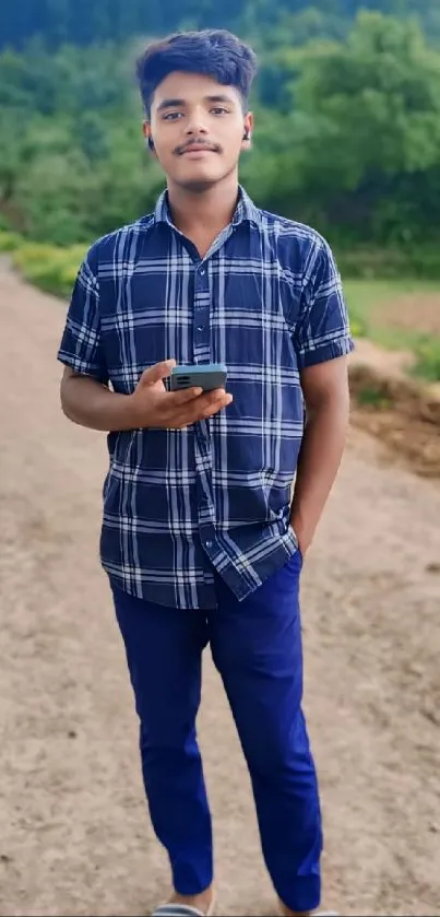 Young boy on a dirt path with greenery, holding a phone.