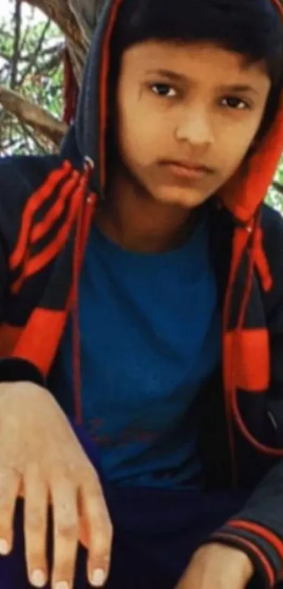 Young boy in a hoodie sitting outdoors.