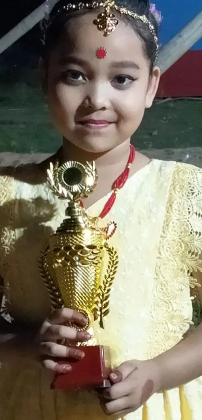 Little girl in yellow dress holding a trophy.