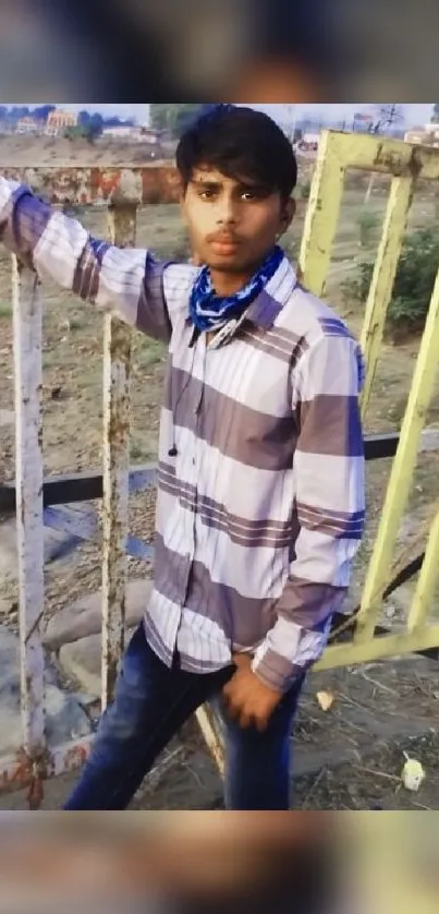 Young man in plaid shirt by a rustic fence.
