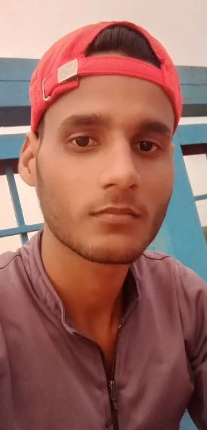 Young man in a red cap sitting outside with a blue fence backdrop.