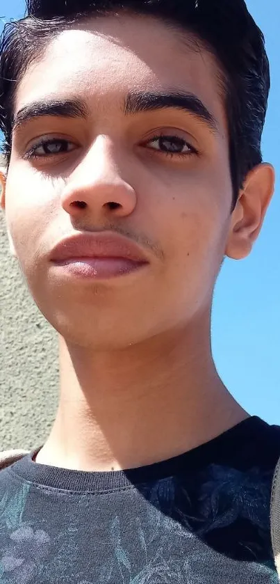 Young man posing outdoors against a sky blue background.