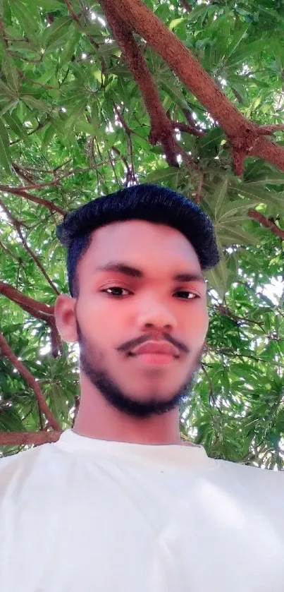 Young man smiles under a vibrant green tree outdoors.