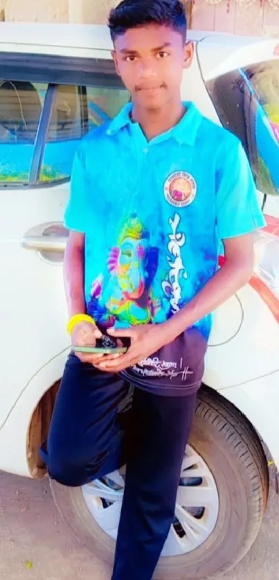 Young man leaning on car in blue shirt.