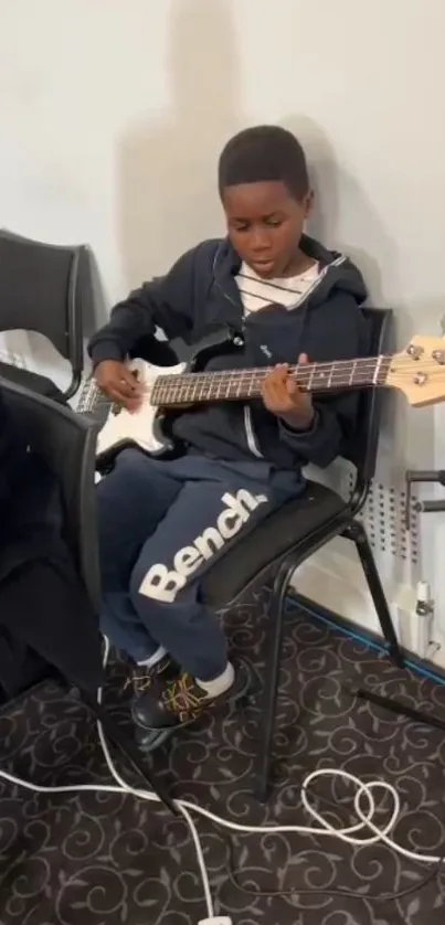 Young boy playing electric bass guitar intensely seated on a chair.