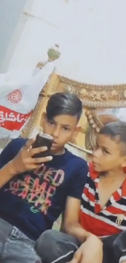 Two boys engaged with a smartphone, sitting casually.