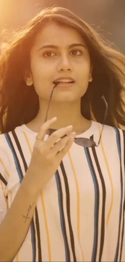 Young woman in striped shirt under sunset light, peaceful expression.