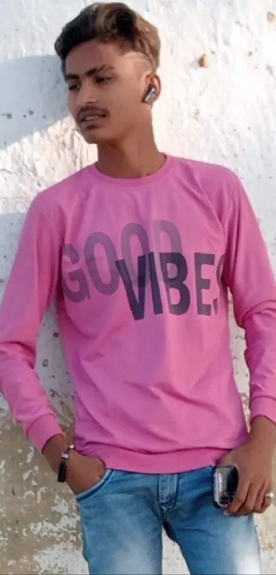 Youthful person wearing a pink 'Good Vibes' shirt against a textured wall.