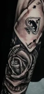 Black and white tattoo featuring rose and ace of spades on arm.