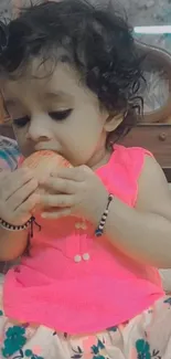 Adorable baby eating apple, wearing pink top.