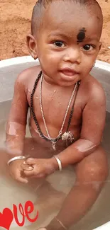 A cute baby sitting in a basin with love text and earthy background.