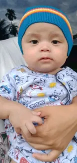 A baby wearing a blue knitted hat and patterned outfit, held in loving arms.