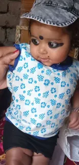 Adorable baby in floral blue outfit and grey cap.