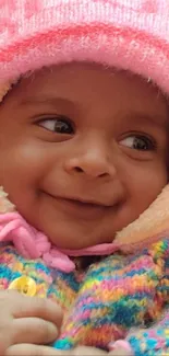 Adorable baby in colorful outfit with pink hat, smiling warmly.