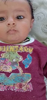 Adorable baby in maroon outfit lying down outdoors.