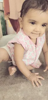 Adorable baby in pink polka-dotted outfit crawling and smiling.