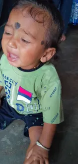 Adorable baby in a green shirt sitting indoors.