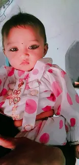 Adorable baby in pink polka dot attire with soft expression.