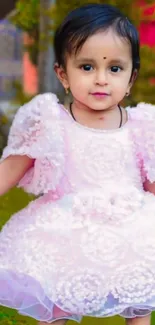 Adorable baby in a pink dress sitting in a garden.