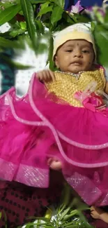 Baby wearing pink dress on a leafy background.