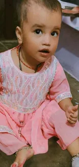 Adorable baby in a pink traditional dress sitting on the floor.