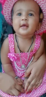 Adorable baby in pink dress and hat, smiling warmly.