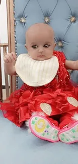 Adorable baby in a red dress on a luxurious chair.