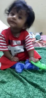 Adorable baby in red outfit sitting on green background with toys.