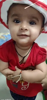 Adorable baby in red outfit and hat, smiling.