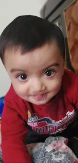 Adorable baby in red sweater smiling playfully at the camera.