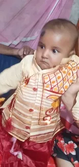 Adorable baby in a traditional outfit, sitting on a vibrant backdrop.