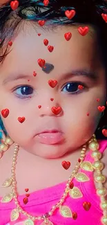 Adorable baby in pink attire with a gold necklace and expressive eyes.