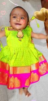 Adorable baby in a bright green and pink traditional dress with golden accents.