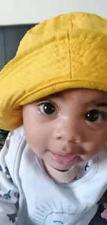 Adorable baby wearing a vibrant yellow hat and smiling.