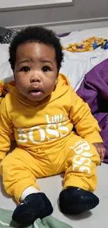 Cute baby in a yellow 'Little Boss' outfit sitting on colorful sheets.