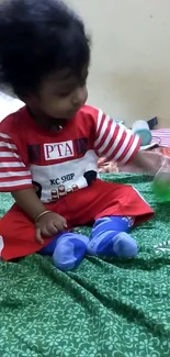 Adorable baby in red outfit on a green patterned blanket.