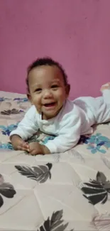 Smiling baby lying on floral bed with pink wall background.