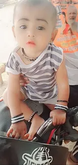 Adorable baby in striped outfit on a motorbike seat.